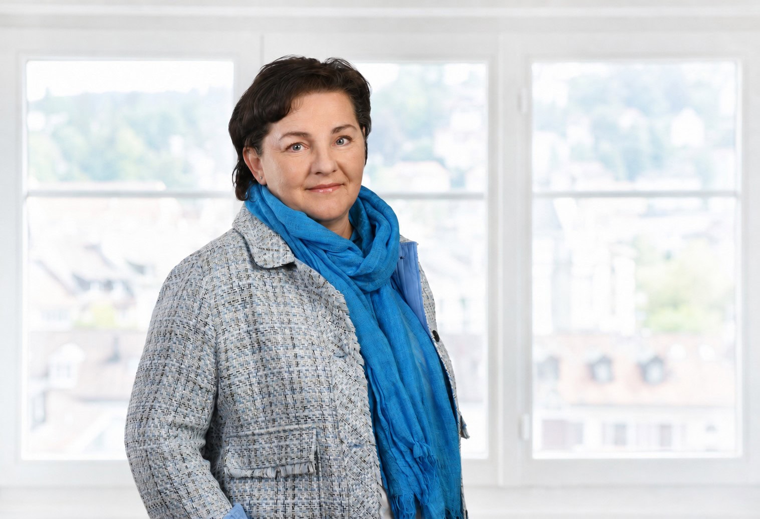 Frau mit blauem Schal vor grossen Fenstern